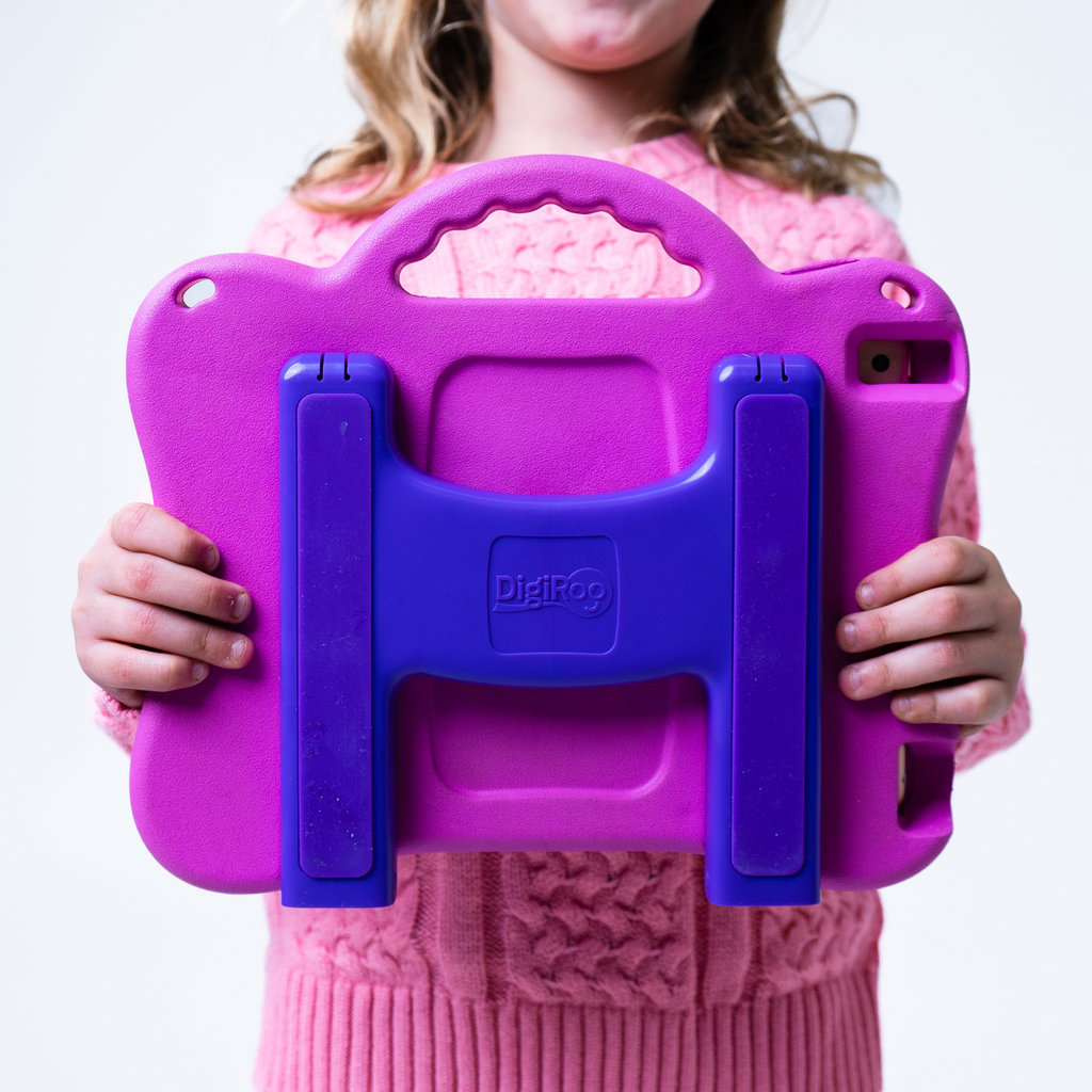 Child holding the pink and purple ipad case. Case is ergonomic, has a handle, and a stand.